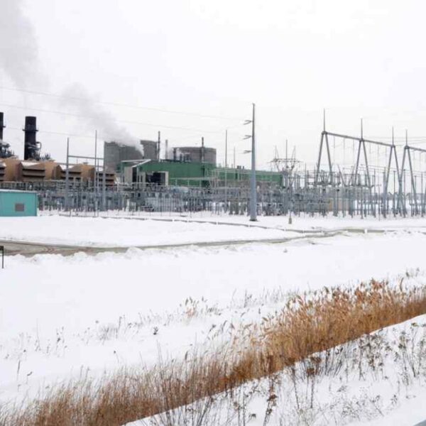 A snowy industrial landscape featuring a power plant emitting steam, with electrical towers and equipment in the background.