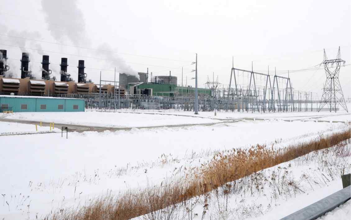 A snowy industrial landscape featuring a power plant emitting steam, with electrical towers and equipment in the background.