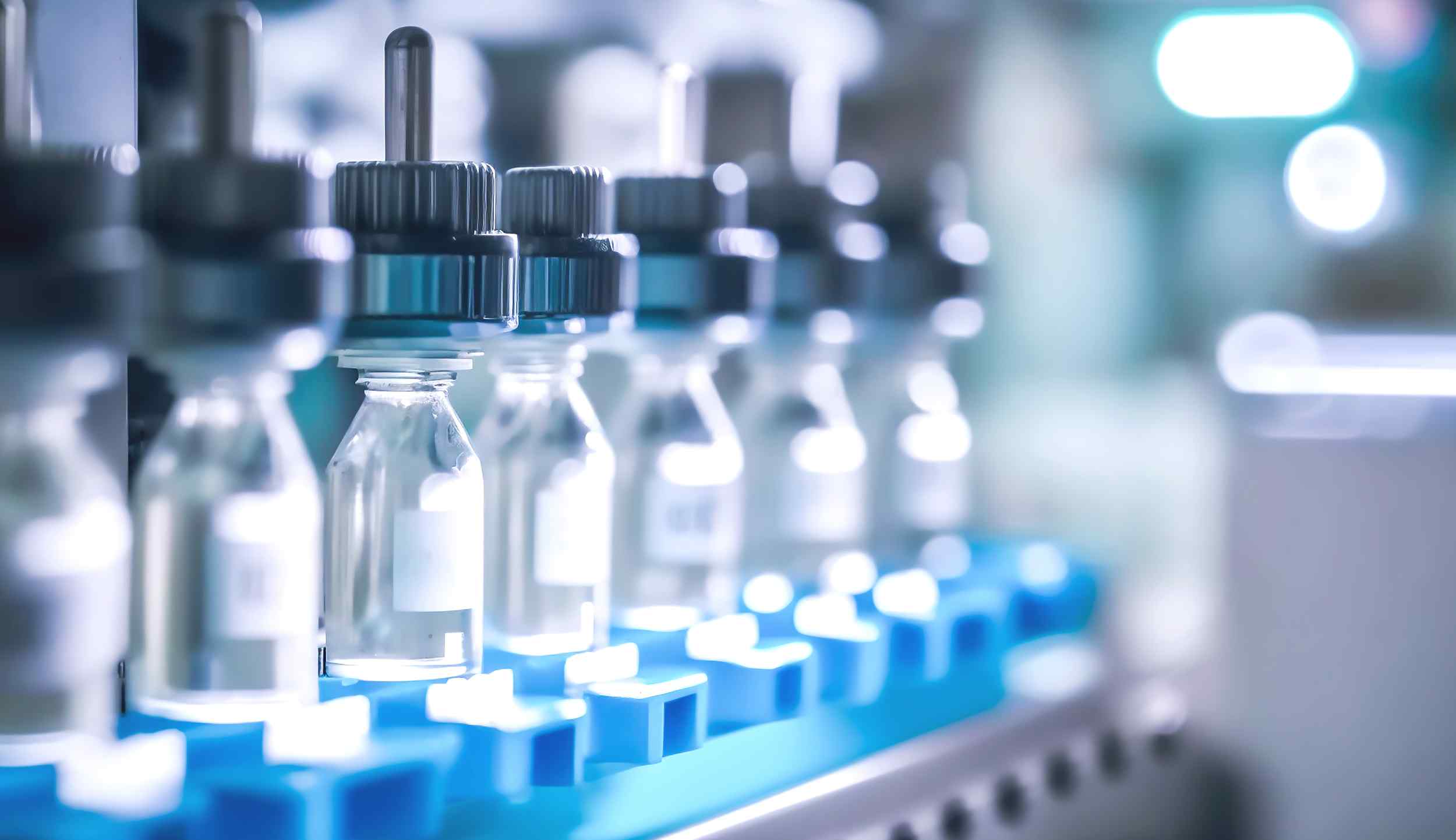 Close-up of sterile glass vials on a blue rack, reflecting soft lab lighting, commonly used for pharmaceutical or laboratory applications.