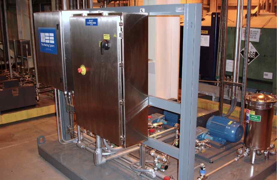 An industrial control panel with metal casing, valves, and pipes, surrounded by machinery, indicating a processing system.