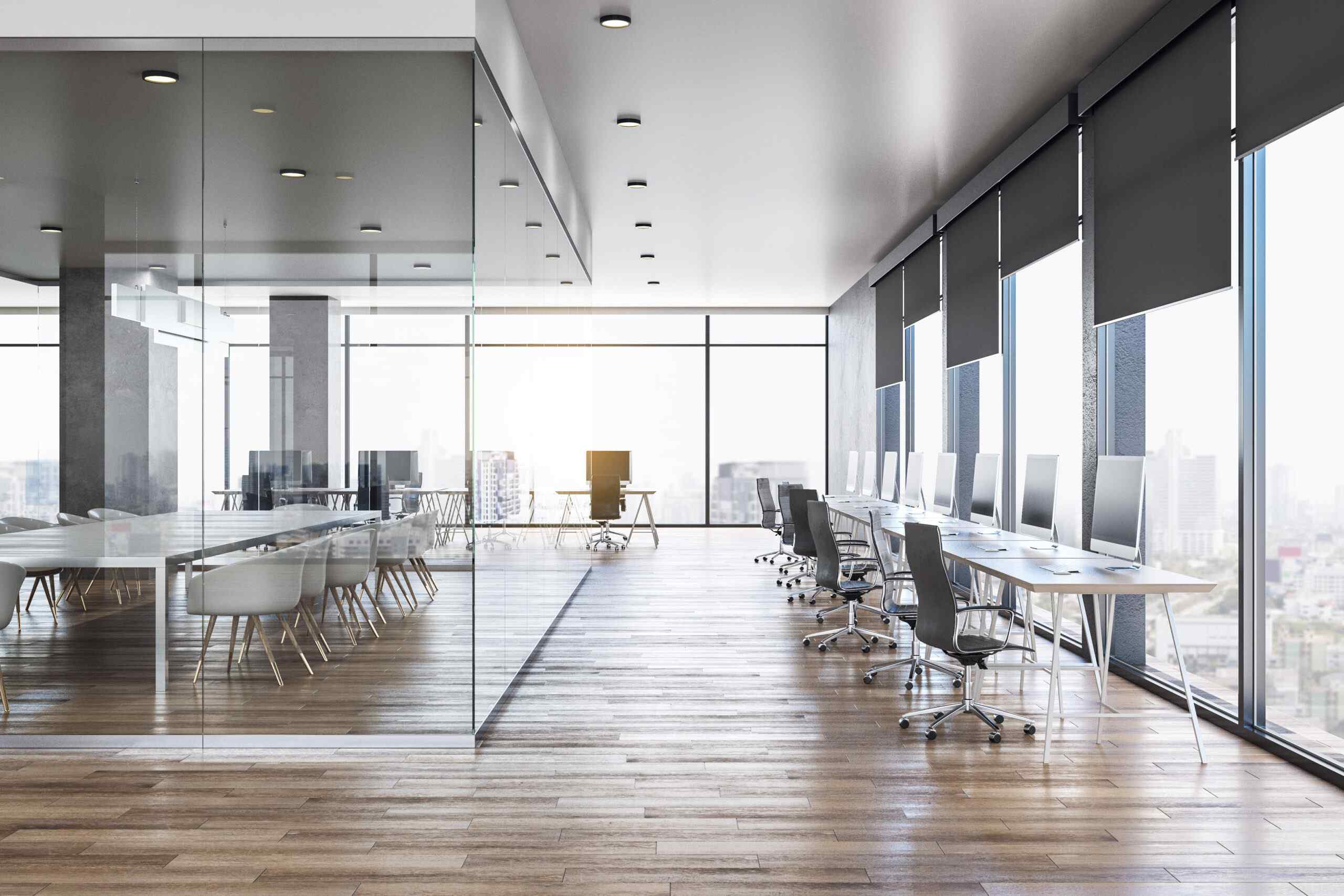 A spacious modern office with glass walls, large windows, and sleek desks equipped with computers, overlooking a city skyline.