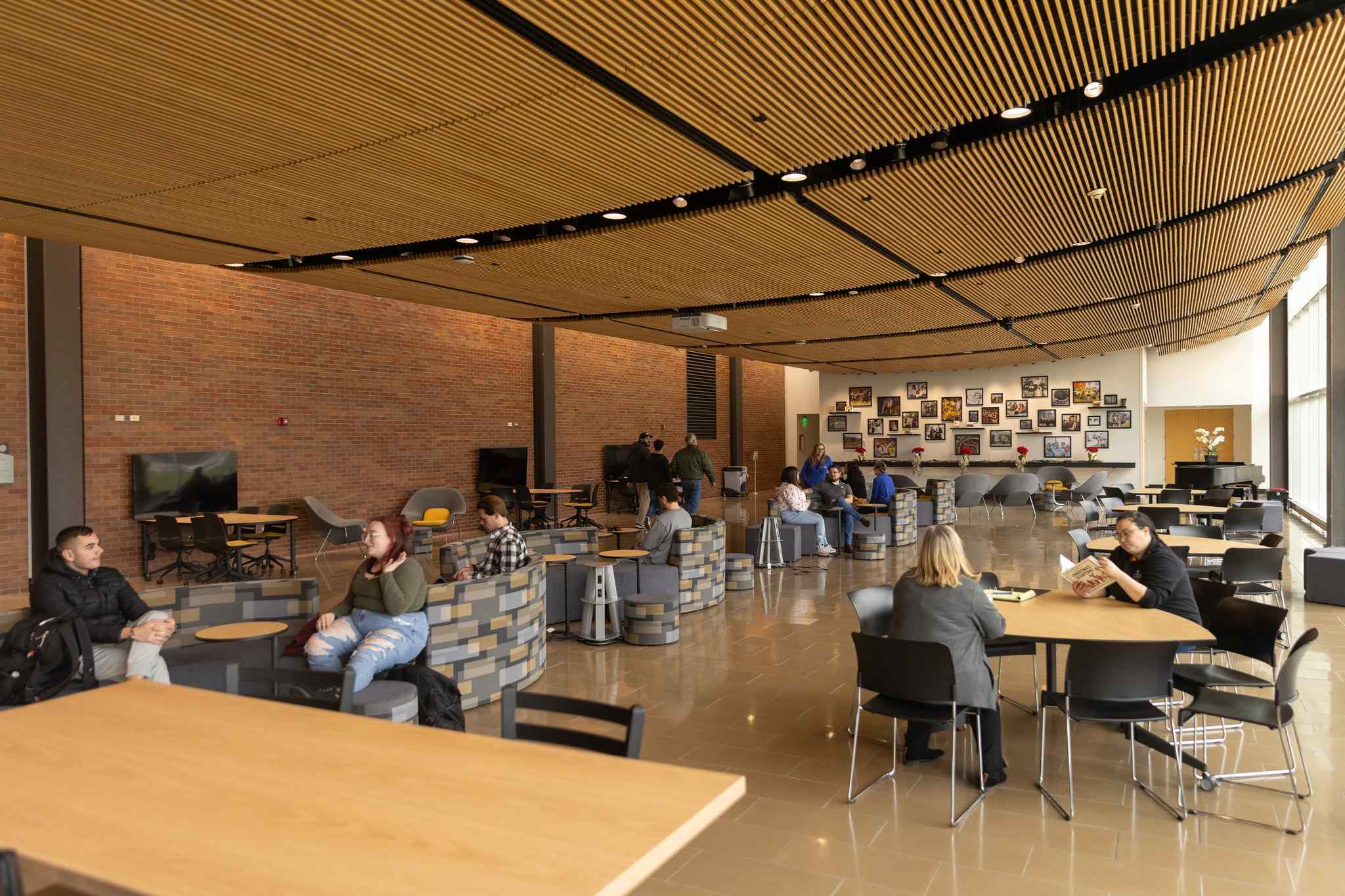 A modern cafe interior featuring a mix of seating arrangements, brick walls, and a decorative photo display. Natural light floods the space.