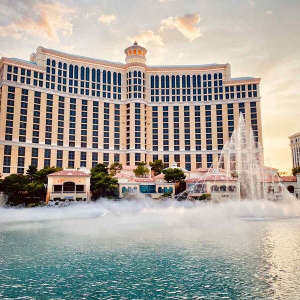 The Bellagio hotel in Las Vegas at sunset, with its iconic fountain display and mist rising from the water.