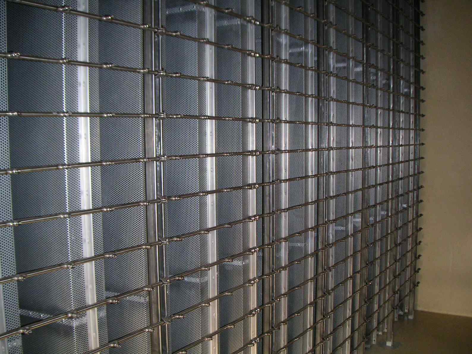 A close-up view of a metallic grid shelving unit with perforated panels, providing organized storage in a dimly lit room.