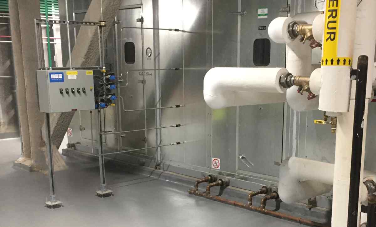 Industrial setup featuring valves and pipes, with a control panel mounted on a wall in a metallic environment.