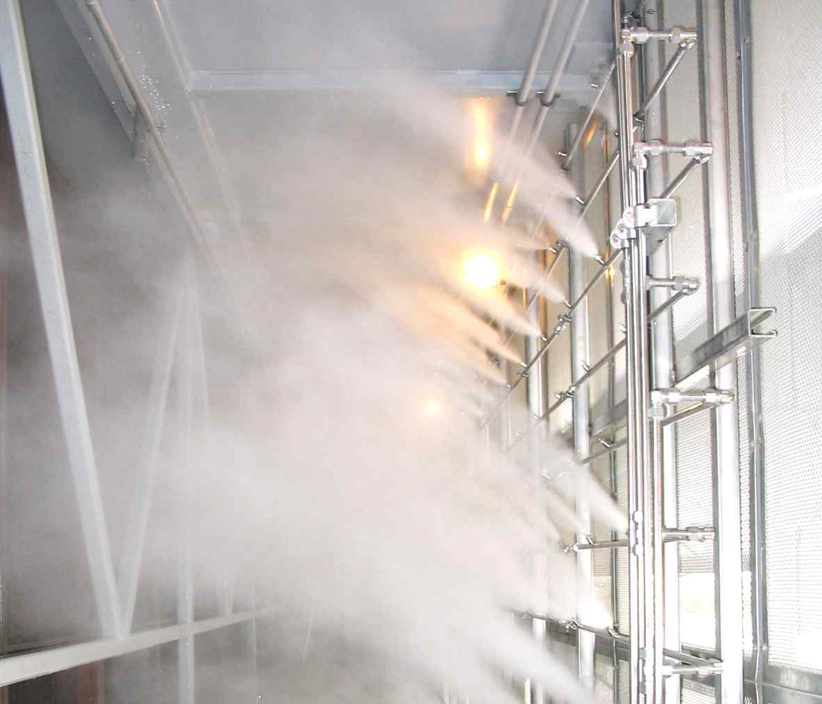 A misting system sprays fine water droplets inside a metallic structure, illuminated by warm overhead lights.