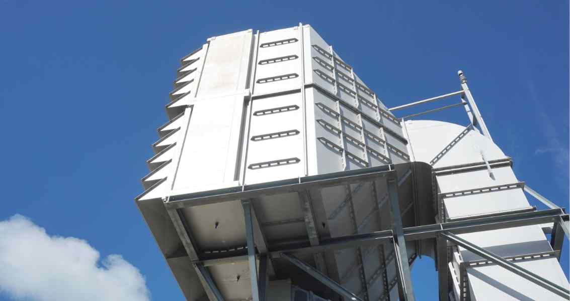 A tall, metallic structure with a series of slanted panels, set against a clear blue sky. Industrial design with a modern aesthetic.