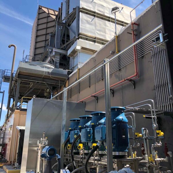 Industrial facility featuring large cooling units and blue pumps with pipes and valves against a clear blue sky.