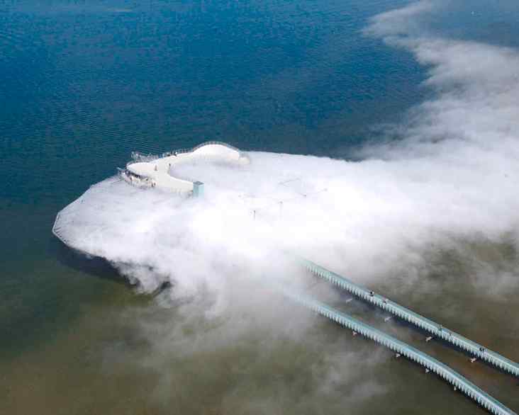 Aerial view of a large, mist-covered structure in water, with pipelines extending into the distance, creating a serene, foggy scene.