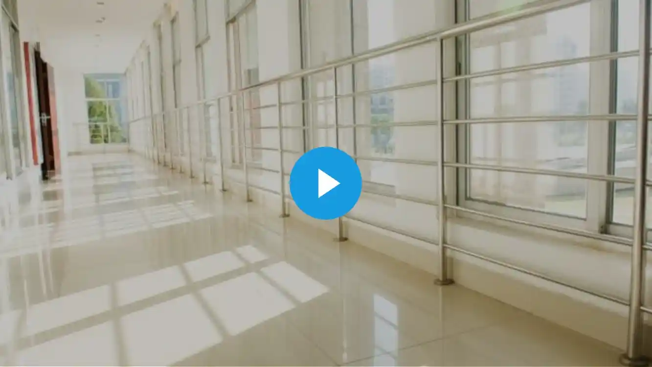 Bright and modern hallway with large windows, polished floors, and a metal railing, featuring a play button in the center.