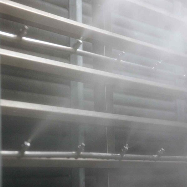 Steam and water mist discharge from metal pipes, creating a foggy atmosphere near horizontal metal shelves in an industrial setting.