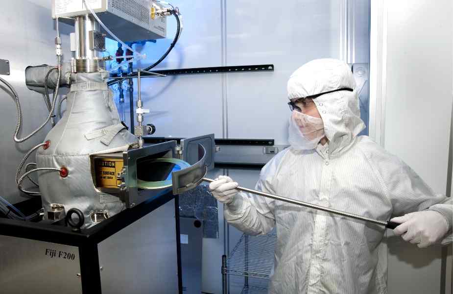 A technician in a cleanroom suit handles equipment inside a laboratory, focused on a process involving a circular object.