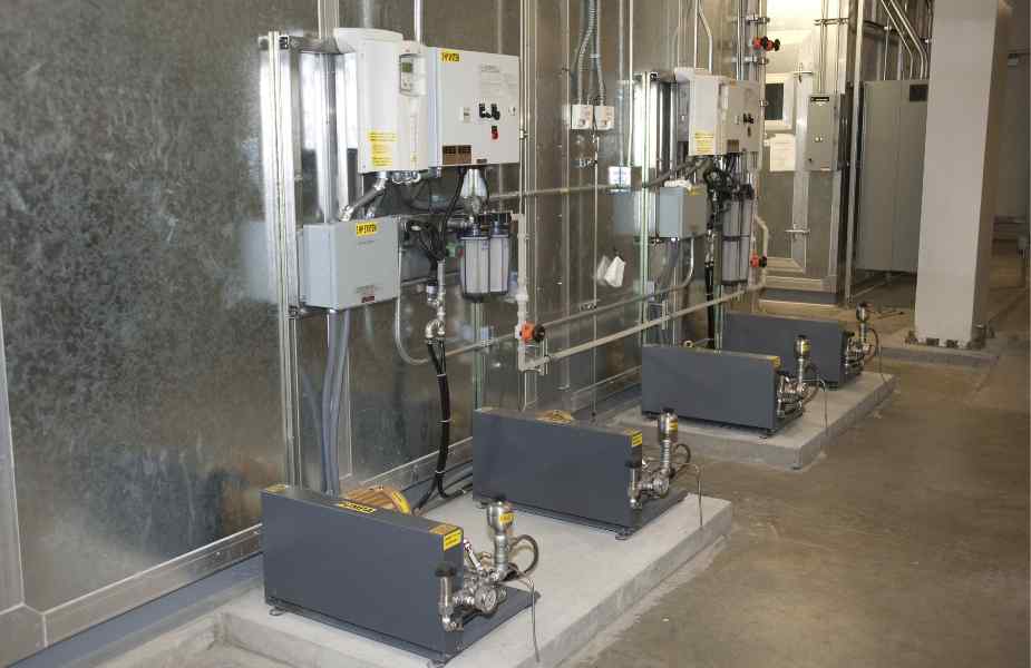 Industrial pumps and control units lined against a wall, connected by pipes in a clean, well-lit facility.