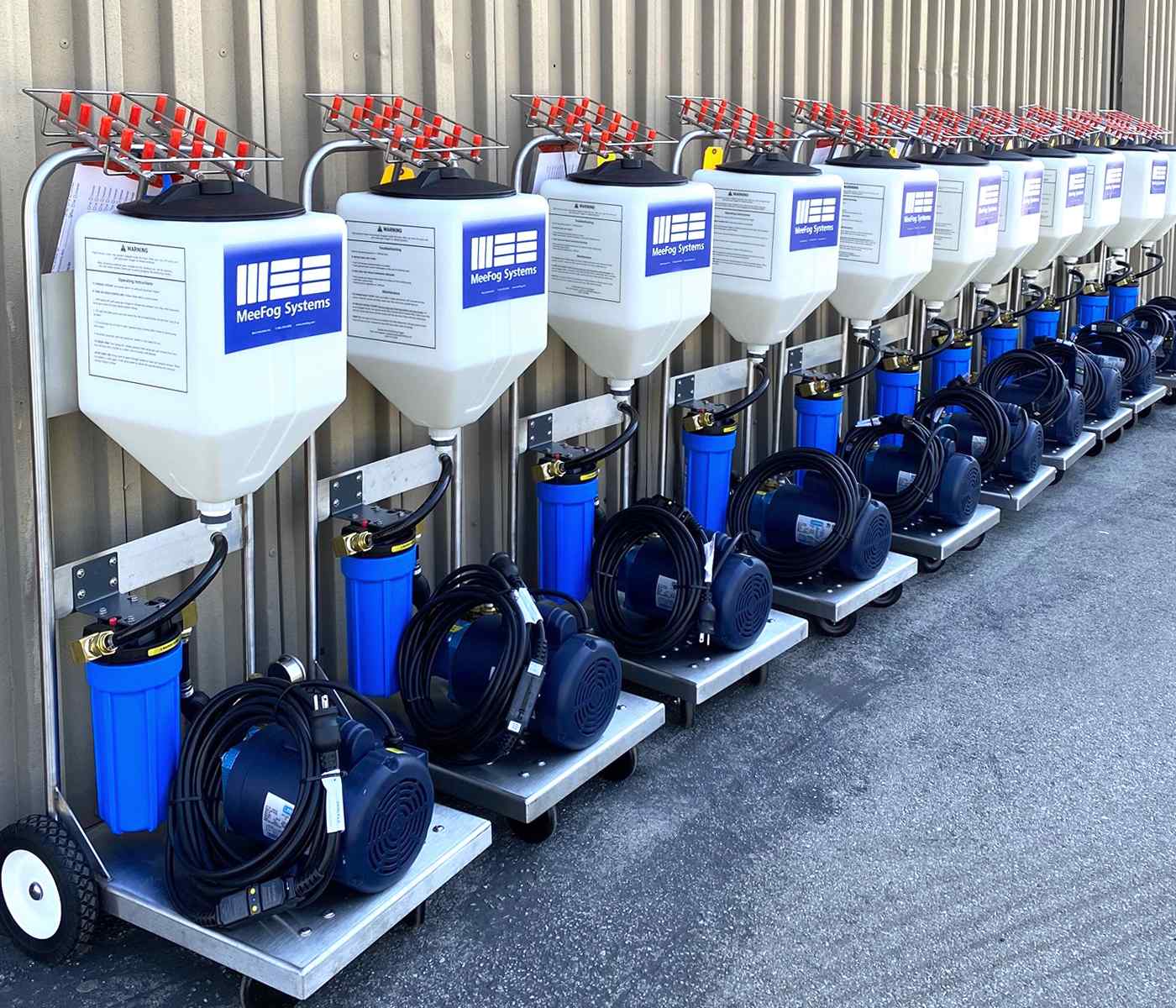 A row of nine MeeFog misting systems with tanks and blue filters, each connected to a black hose, efficiently lined up.