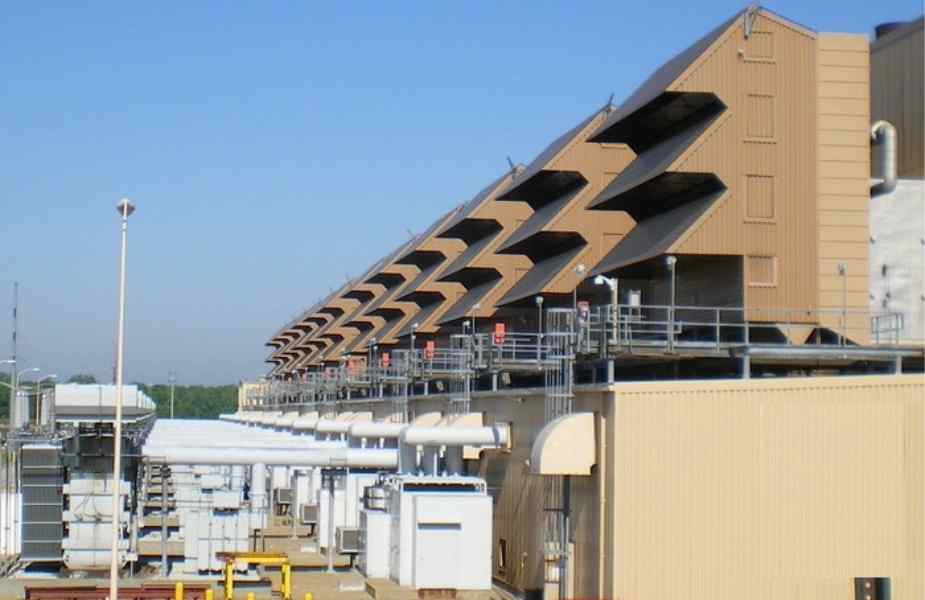 Industrial facility with brown angular structures and pipes, set against a clear blue sky, indicating a working environment.