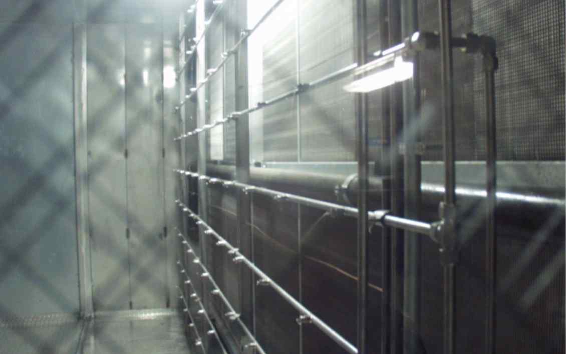 Interior of a hallway with metal mesh fencing, illuminated by overhead lights, showcasing a streamlined, industrial design.