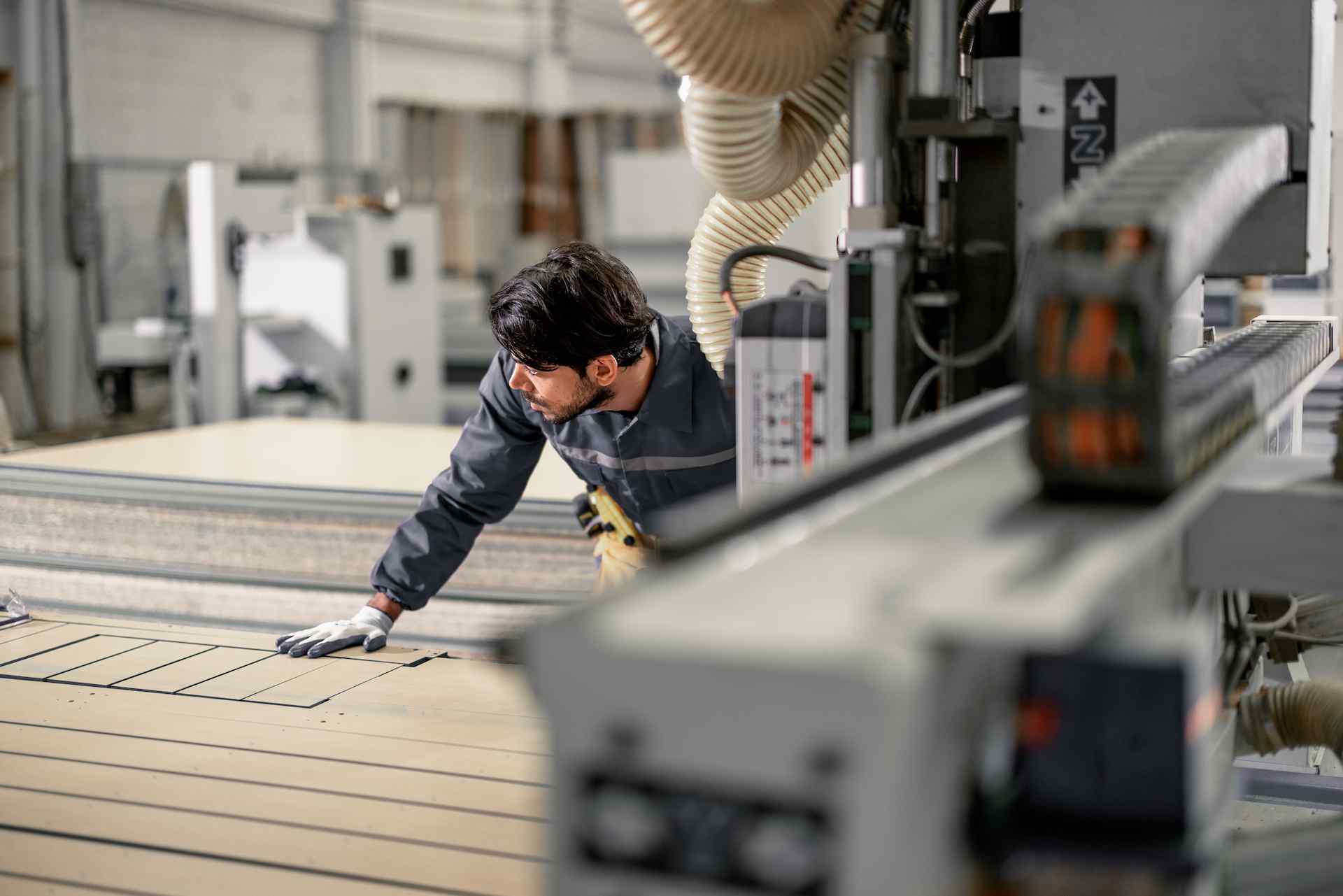 A worker inspects a large wooden panel on a CNC machine in a well-lit workshop, demonstrating precision in craftsmanship.