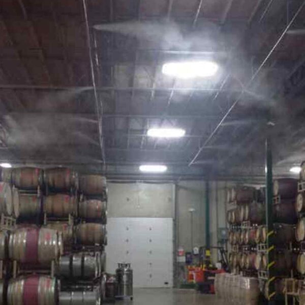 A dimly lit storage facility with stacked wooden barrels, mist rising from the ceiling, and a large white door in the background.