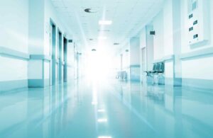 Bright hospital corridor with polished floors, empty waiting area chairs, and softly illuminated walls leading to a glowing exit.