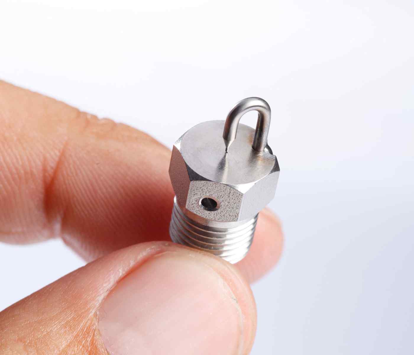 Close-up of a person's finger holding a metallic nozzle, showcasing its threaded base and a bent tip for fluid delivery.