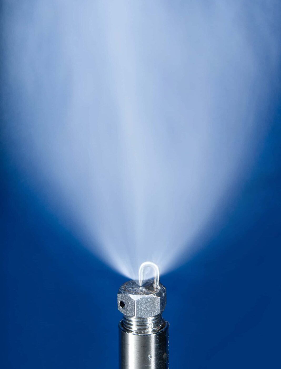 Stainless steel impaction-pin nozzle spraying a fine 20-micrometer mist for industrial humidification.