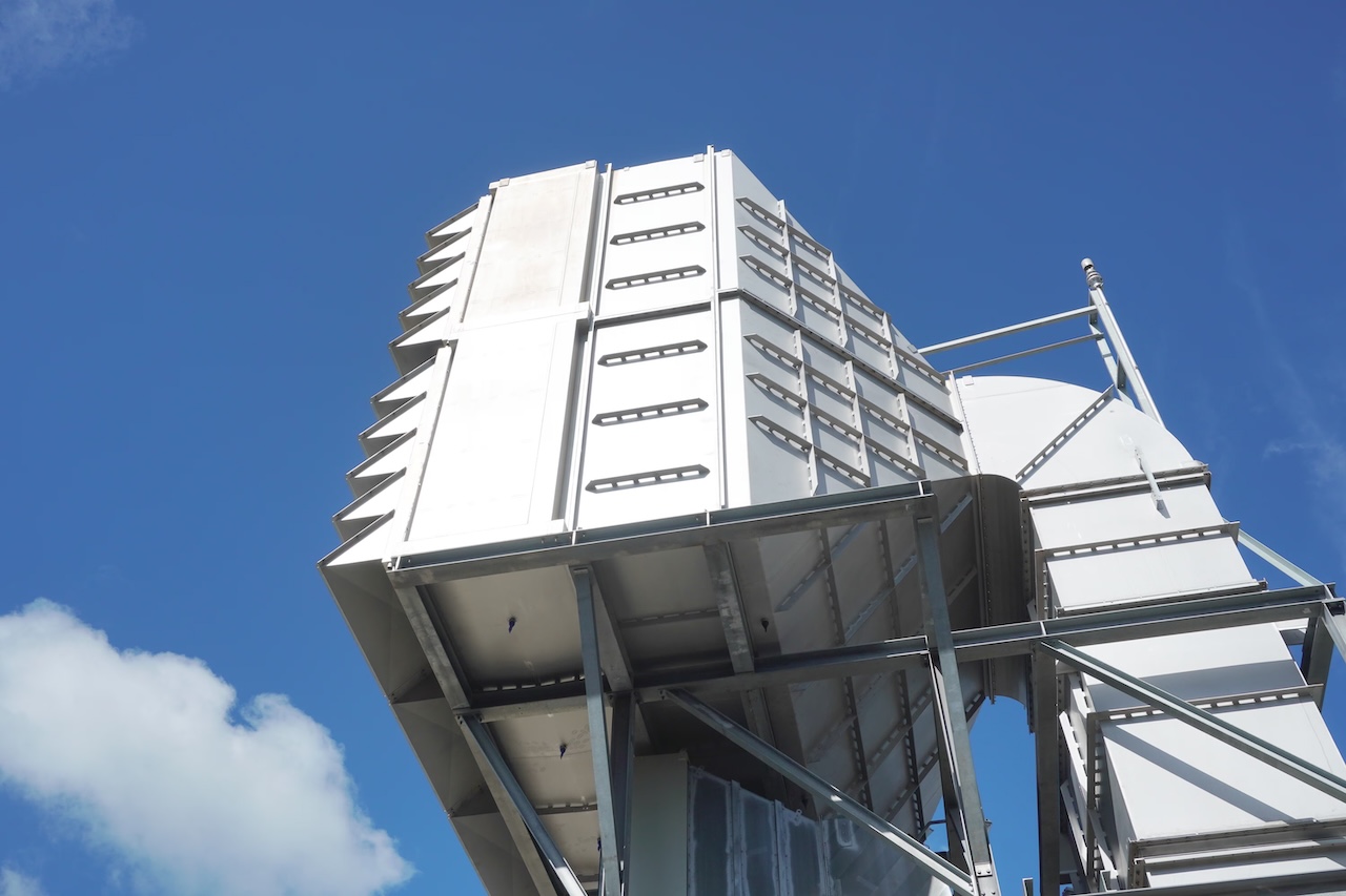 A tall, metallic structure with a series of slanted panels, set against a clear blue sky. Industrial design with a modern aesthetic.