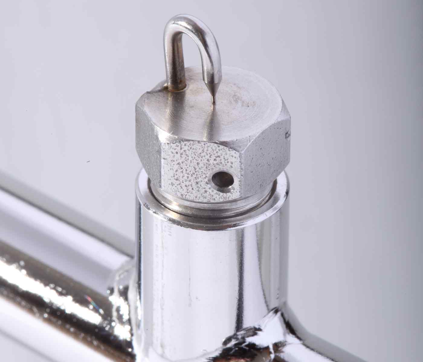 Close-up of a metal valve featuring a hexagonal top and a small hook, polished chrome finish with visible threading and an opening.