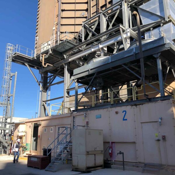 Industrial facility featuring a large tower, metal structures, and two workers in safety gear against a clear blue sky.