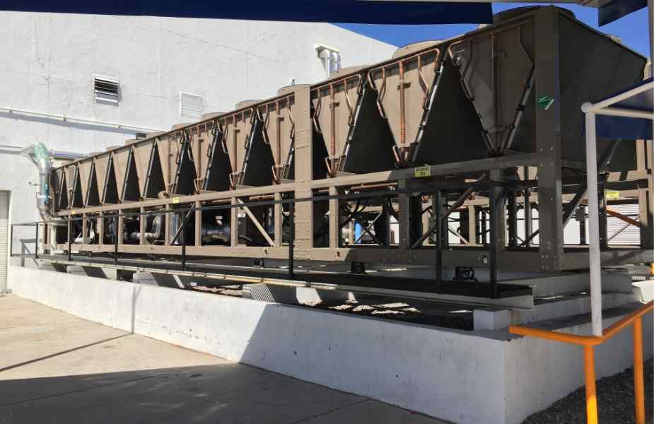 Large industrial cooling system mounted on a concrete platform, featuring multiple triangular cooling towers and visible piping.