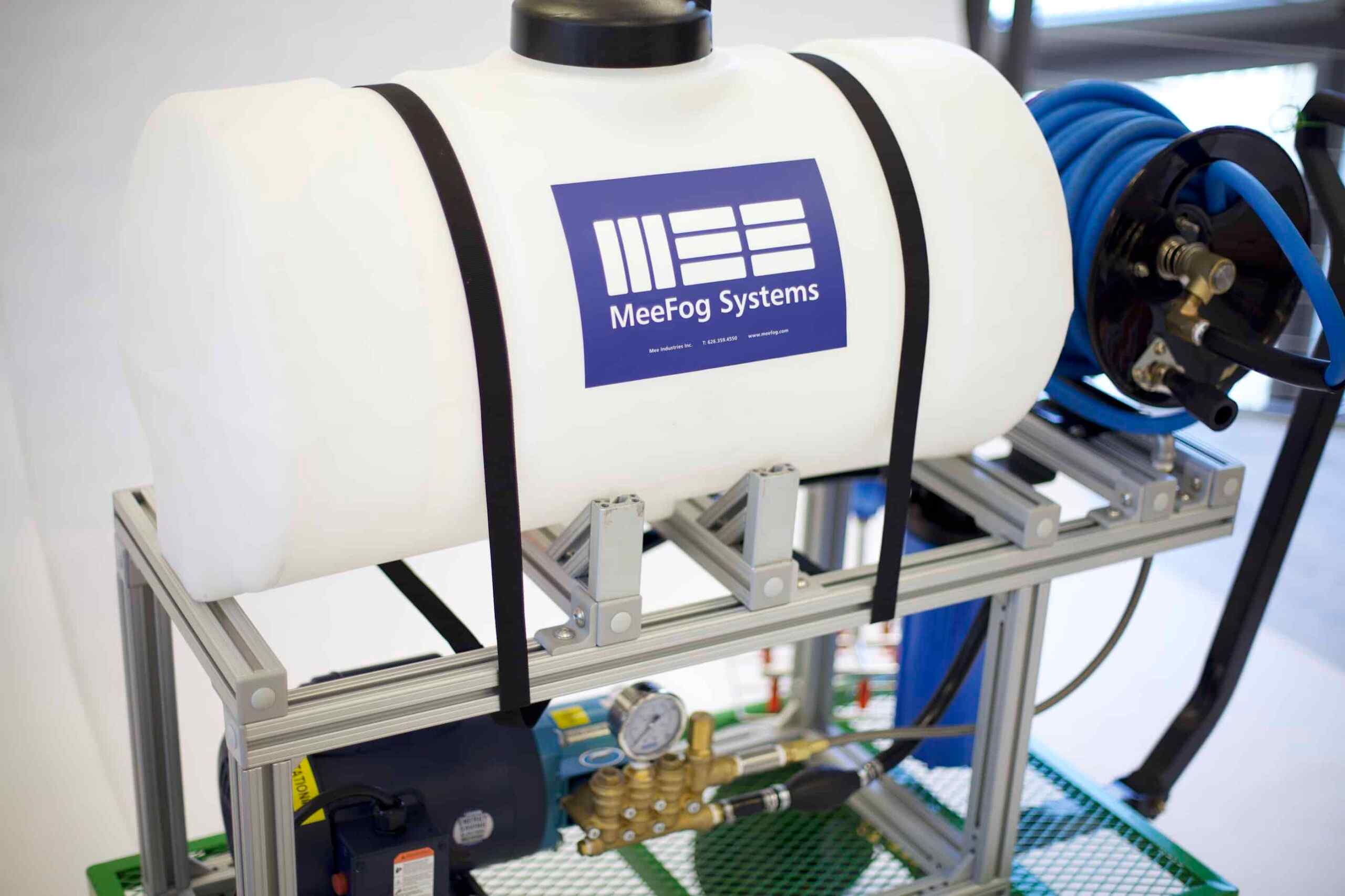White water tank on a metal frame marked "MeeFog Systems," with blue hoses and mechanical components visible in the setup.
