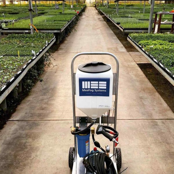 A fogging machine with a MeeFog Systems logo sits on a path surrounded by rows of vibrant, growing plants in a greenhouse.