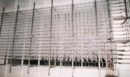 Industrial ice-making machine with a grid of metal pipes and hanging ice forms, showcasing a large quantity of ice being produced.
