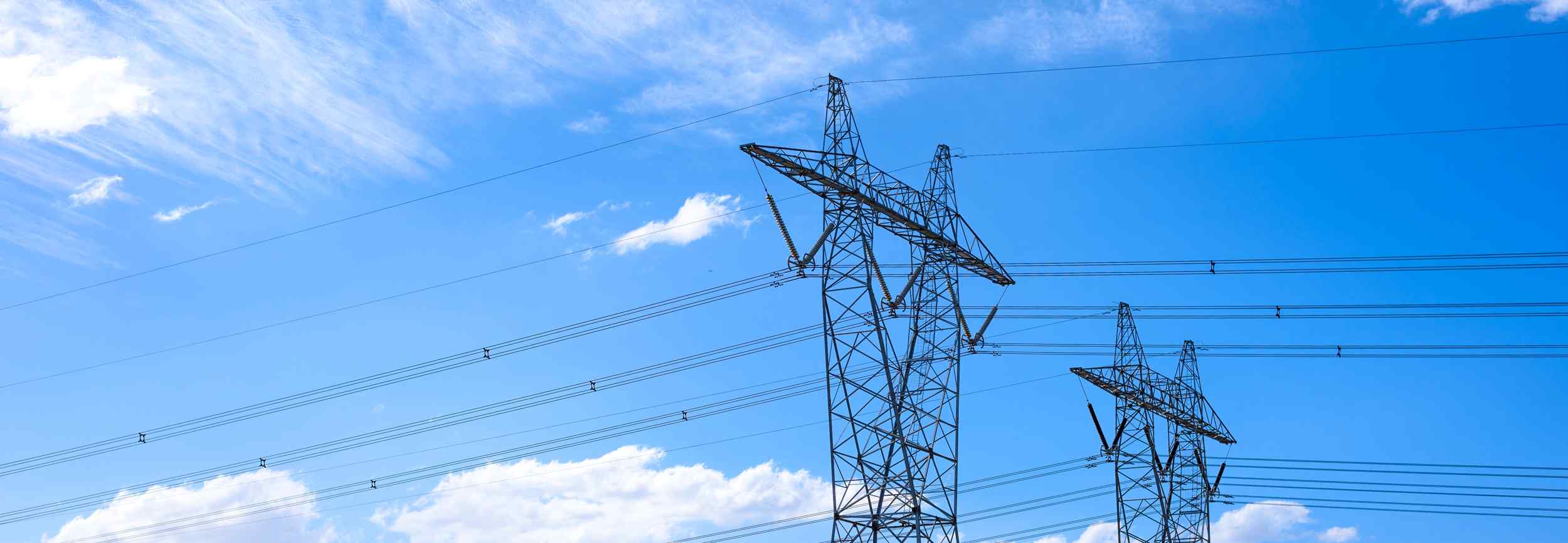 Two tall transmission towers with power lines against a bright blue sky with scattered clouds.