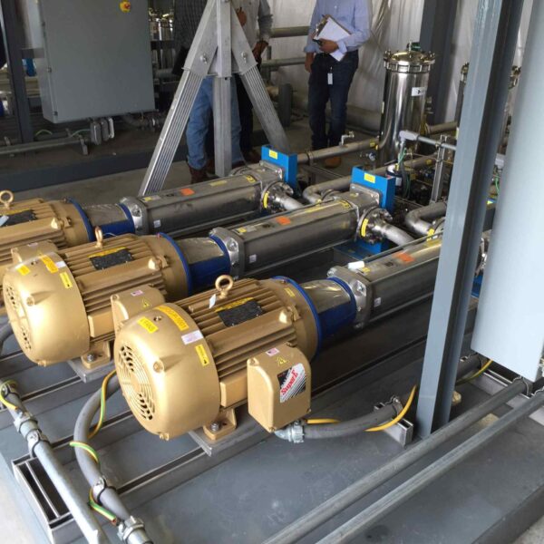 A collection of industrial pumps and motors in a facility, with pipes and a control panel visible in the background.
