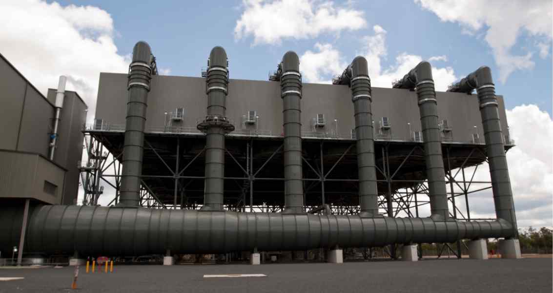 Industrial power plant with tall, cylindrical exhaust stacks and large, curved pipelines, set against a cloudy sky.