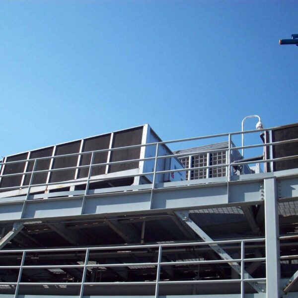 View of a rooftop cooling system with large air conditioning units and a crane, set against a clear blue sky.