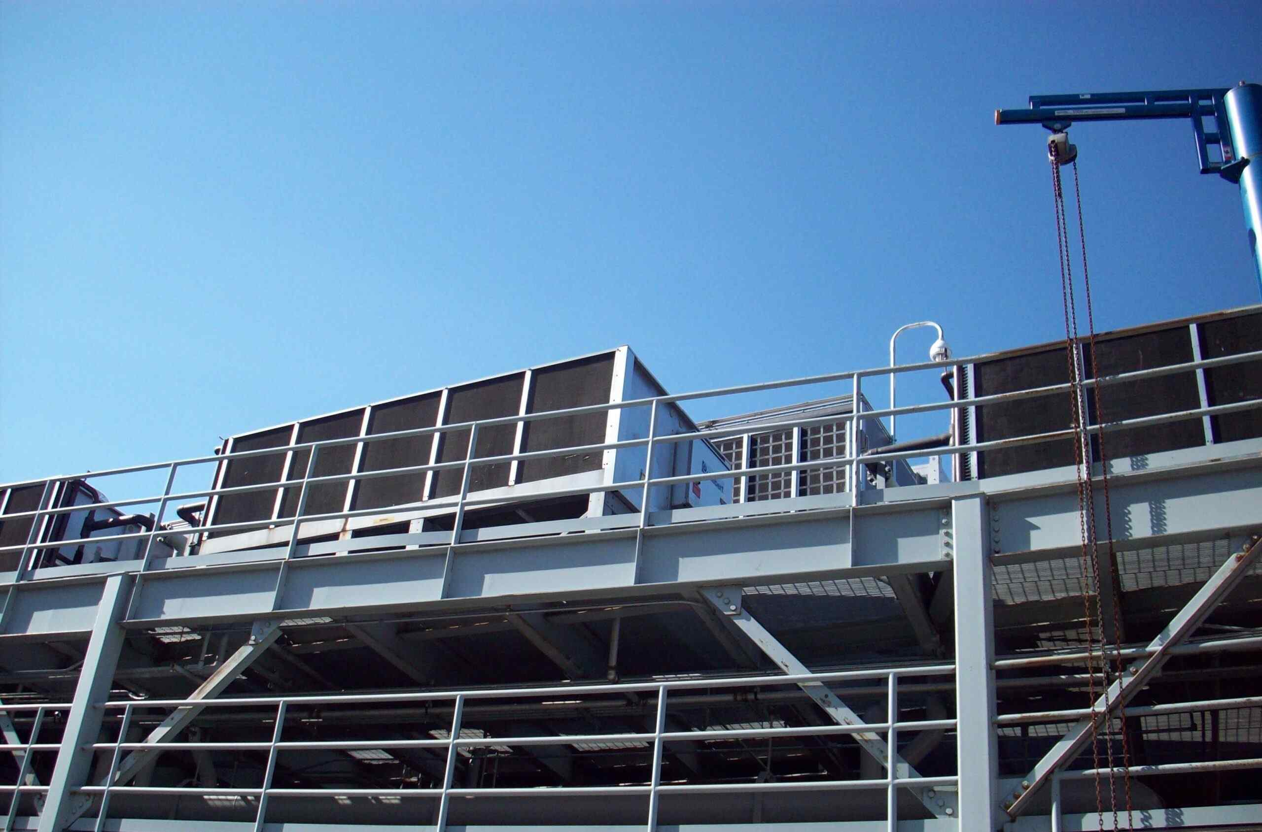 View of a rooftop cooling system with large air conditioning units and a crane, set against a clear blue sky.