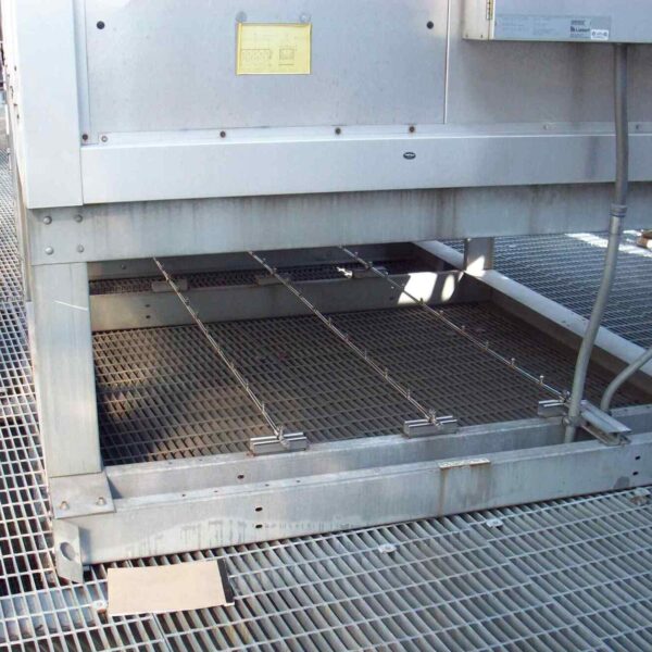 A close-up of the base of an industrial unit on a metal grating platform, featuring metallic supports and visible wiring.