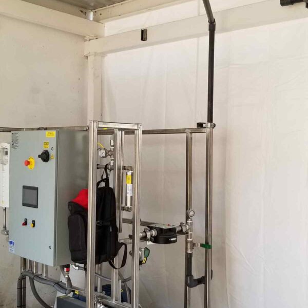A metal frame houses industrial equipment, including a control panel and pipes, set against a plain white backdrop.