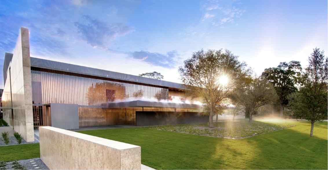 Modern architectural building with sleek metallic facade, surrounded by green lawns and trees at sunset, casting soft light.
