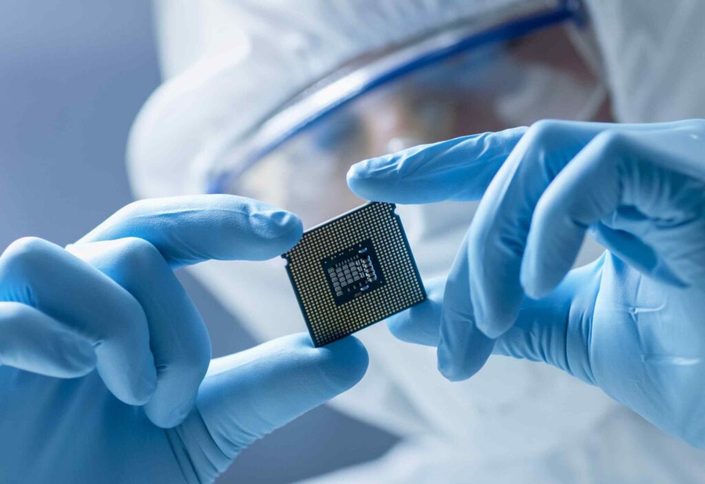 A person in a protective suit holds a microprocessor carefully, showcasing its intricate design against a blurred background.