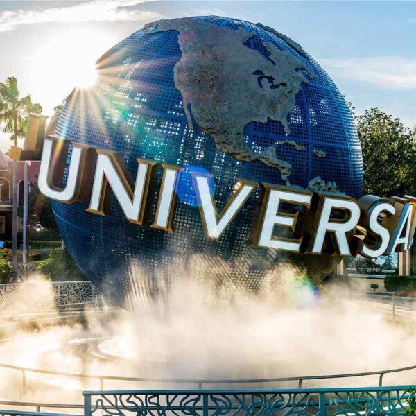 A large, illuminated globe with "UNIVERSAL" prominently displayed, surrounded by mist, set against a bright sky and palm trees.
