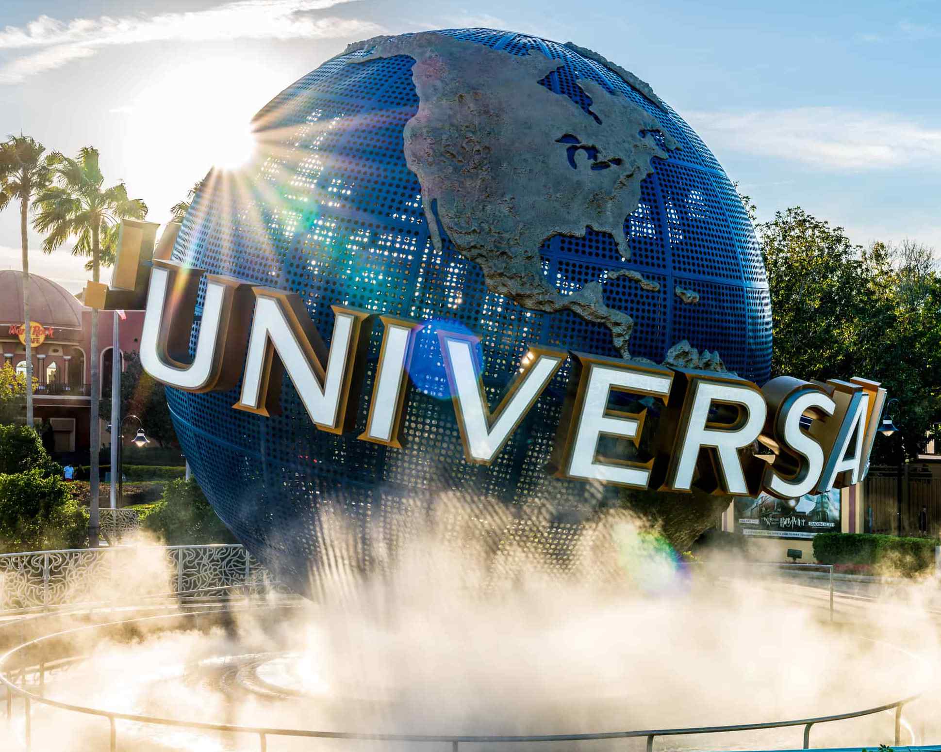 A large blue globe surrounded by mist, featuring "UNIVERSAL" in bold letters, set in a sunny theme park environment with palm trees.