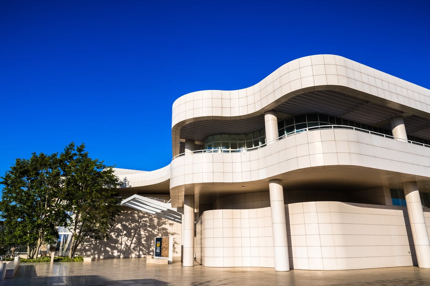 Exterior view of the white curved travertine stone architecture and modern glass facade of the Getty Center entrance hall under a clear blue sky.